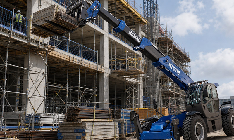 HT6018 telehandler extending its boom to lift formwork panels and rebar bundles to an upper floor on a high-rise construction site.